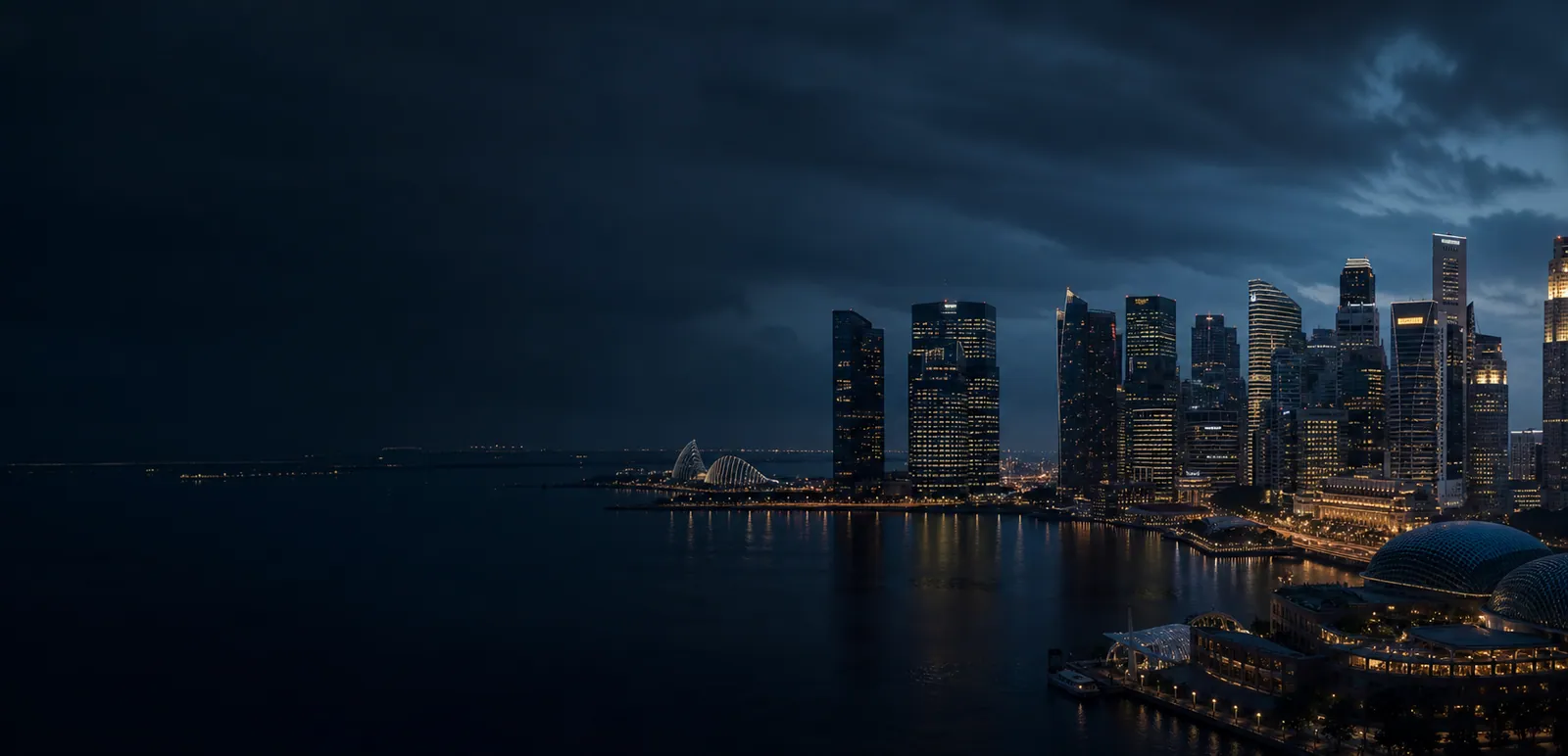 Singapore waterfront skyline illuminated at night beneath a deep blue sky.